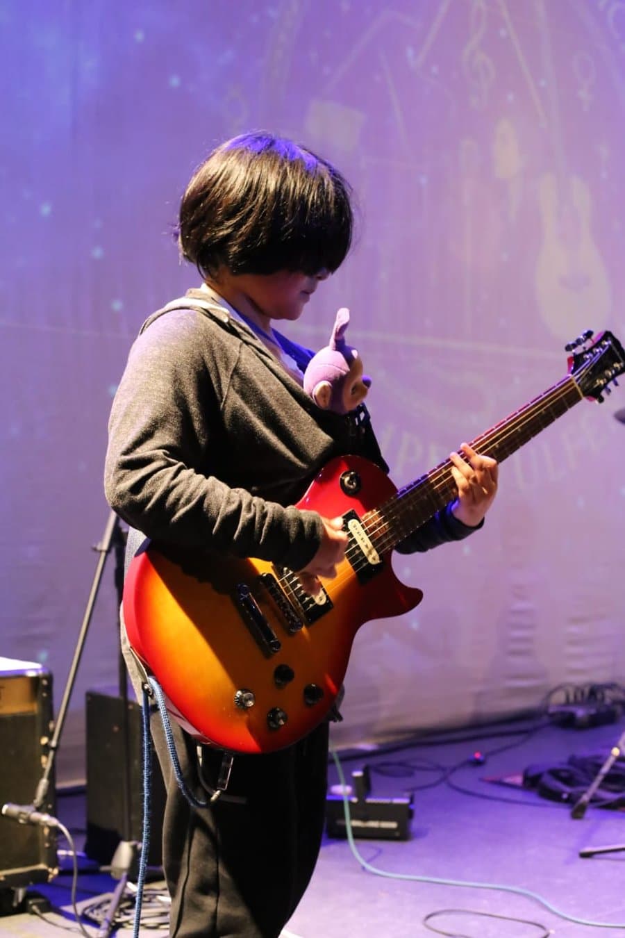 Alumno con guitarra eléctrica y un peluche colgado